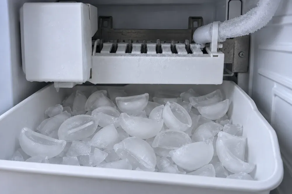 Ice maker with a frost-covered fill tube above a bin of crescent ice cubes, several hollow