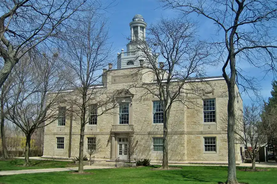 Stone Highland Park City Hall with a cupola behind bare spring trees, Illinois
