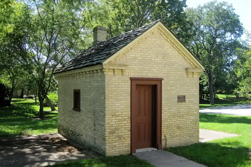 Small yellow-brick Sunderlage Farm smokehouse under shade trees in Hoffman Estates, Illinois