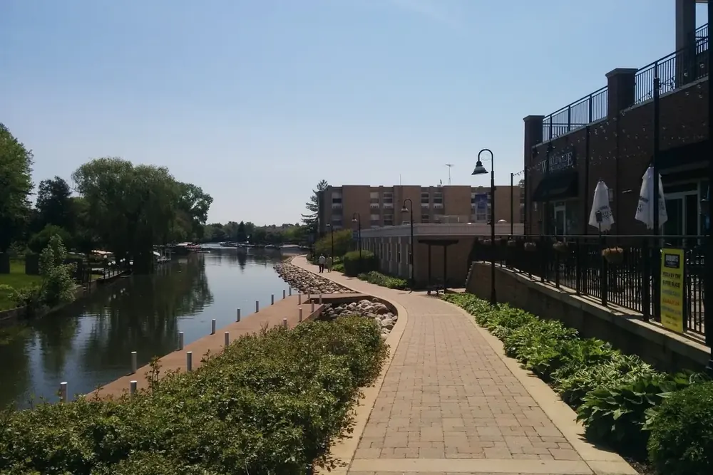 Brick riverwalk path beside the Fox River and landscaped shrubs in McHenry, Illinois