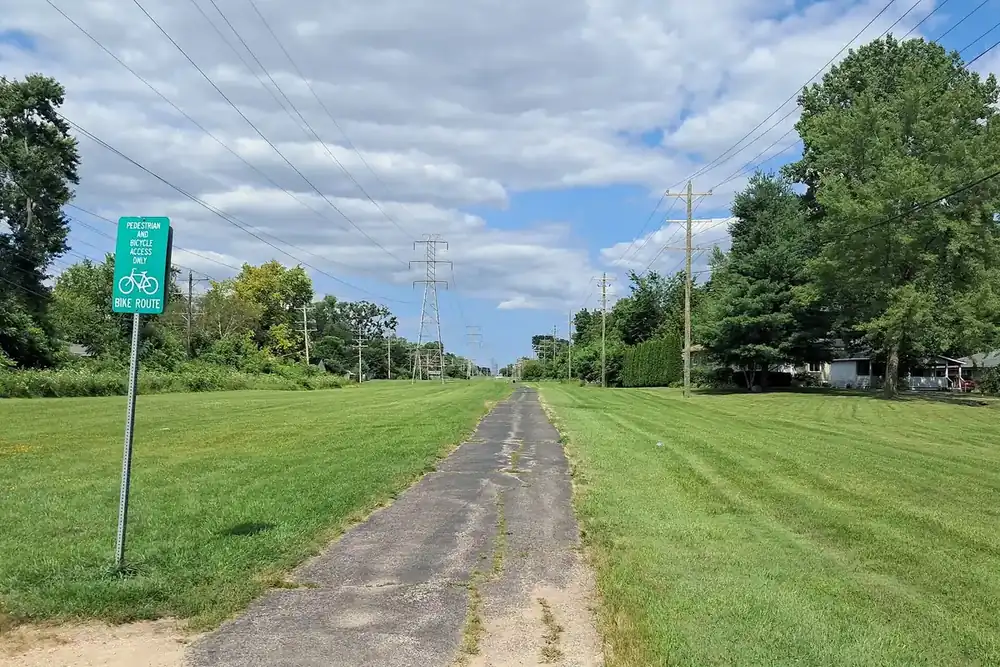 Paved Millennium Trail running through open grass under summer clouds in Round Lake Beach